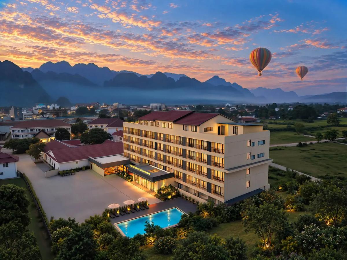 Aerial view of Vangvieng Thavikun Hotel at sunset, with karst mountains and hot-air balloons